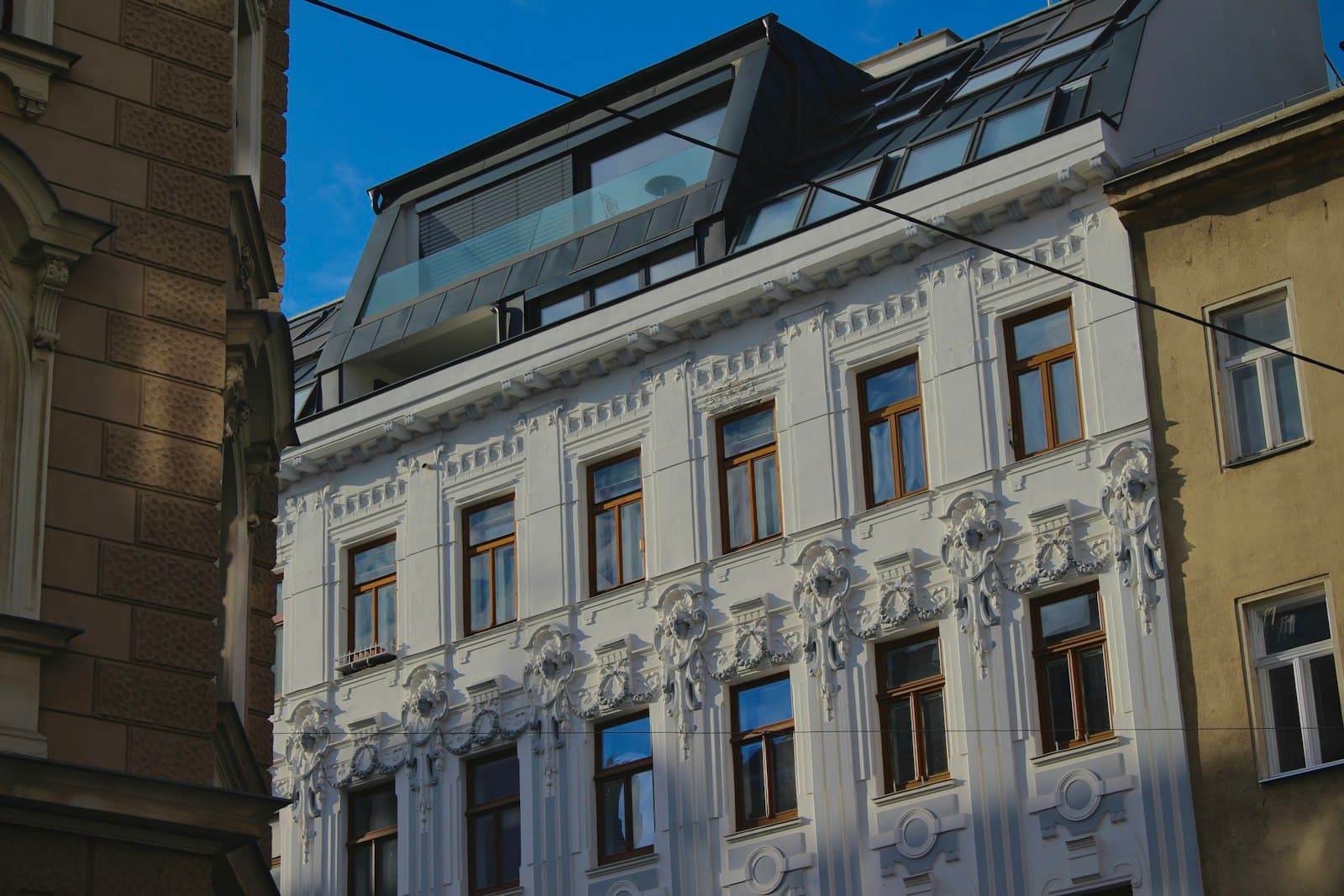 Renovated late-19th-century facade with stucco ornament, timber windows and a converted roof storey next to unrenovated period buildings, photo