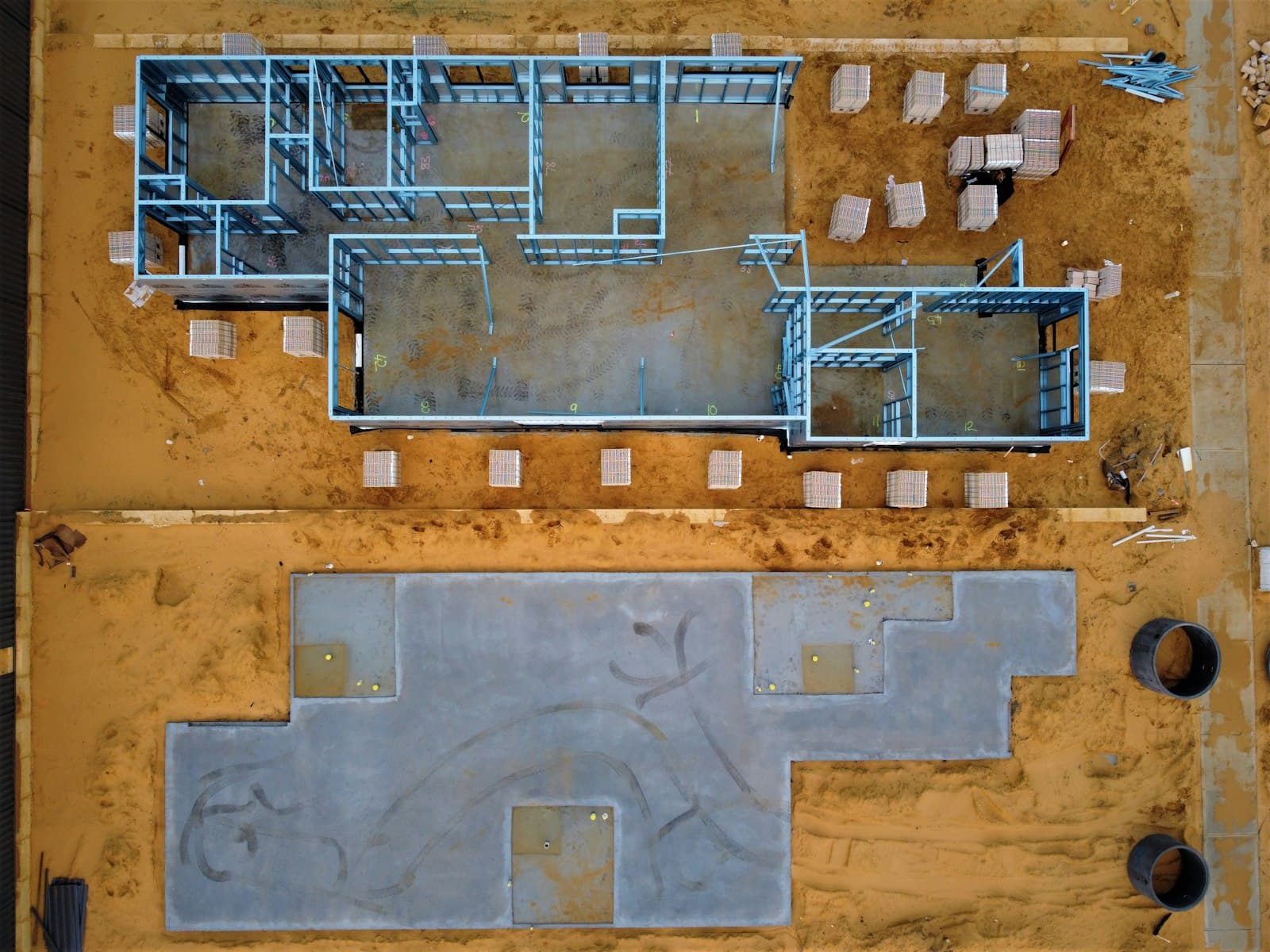 Aerial view of a construction site with two ground slabs, one freshly cast, one with walls starting to rise, photo