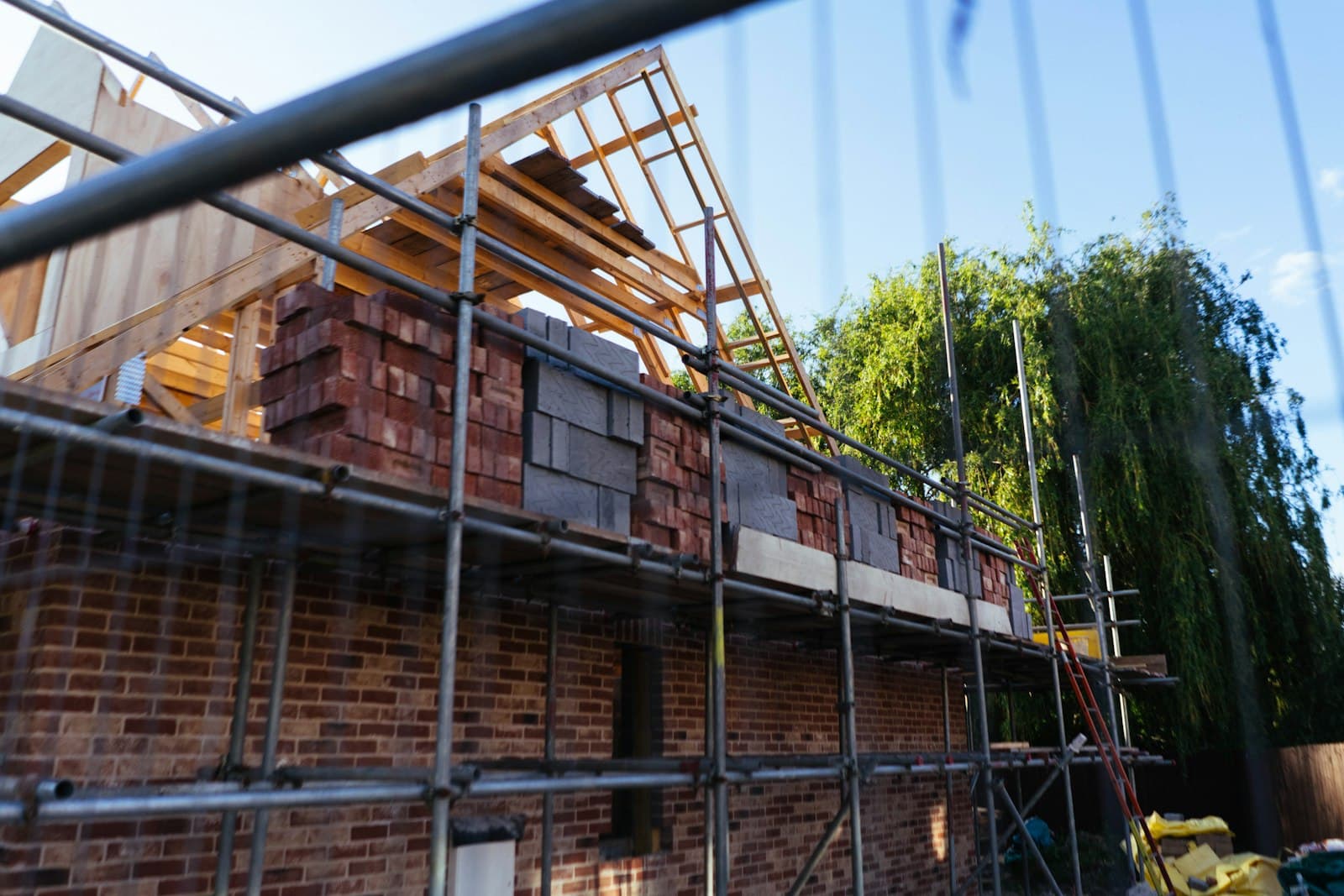 Rohbau eines Wohnhauses mit Ziegelmauerwerk, Gerüst und hölzernem Dachstuhl auf der Baustelle, Foto