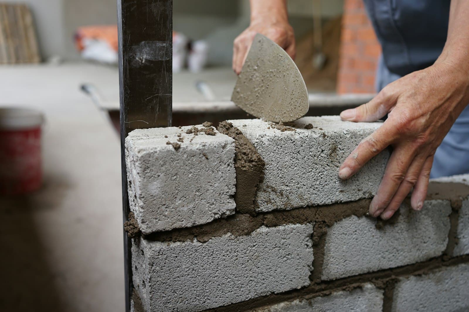 Maurer setzt Betonsteine mit Kelle und Mörtel auf eine Rohbauwand, Foto